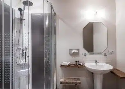 Badkamer met een glazen douchecabine, een witte wastafel en houten planken